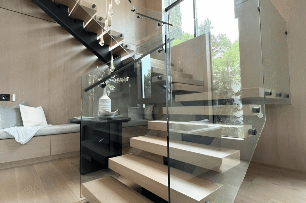 Custom glass stair railing with black standoff hardware and wood floating treads in warm modern indoor living space interior
