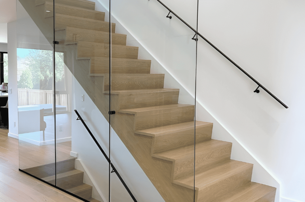 Frameless interior glass stair railing with matte black wall handrail and oak treads in modern open plan home interior design