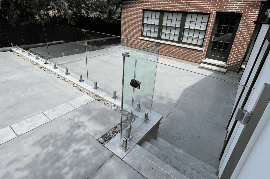 Corner detail of custom glass panels with stainless spigots on concrete patio showing residential glass railing panel design