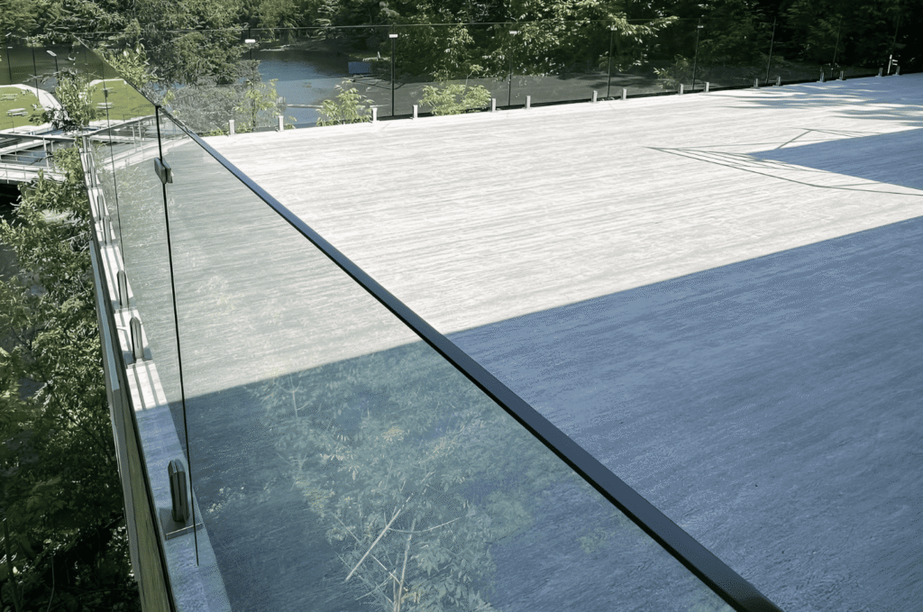 Frameless glass railing with black top rail on stone deck with forest and waterfront view showing outdoor glass railing style