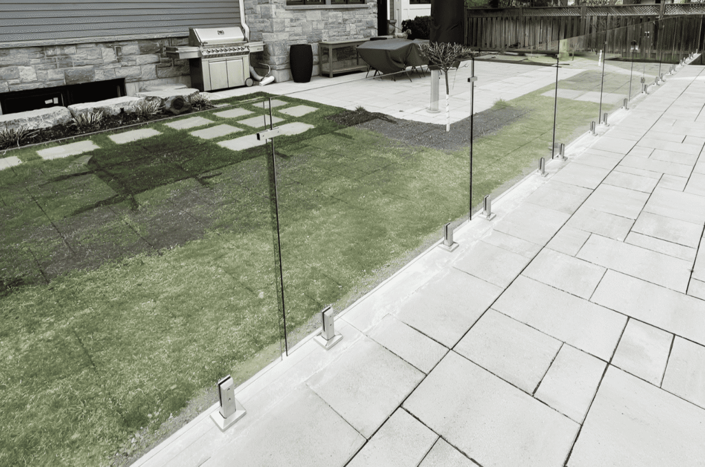 Frameless glass railing system with stainless spigot hardware on stone patio showing exterior glass railing design options