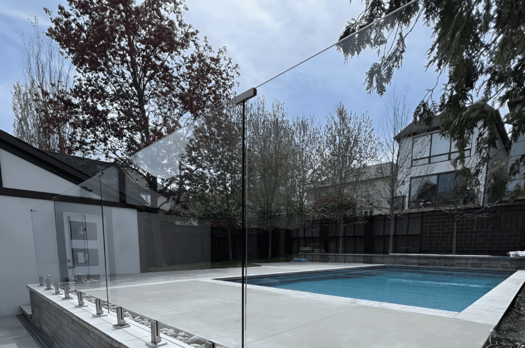 Frameless glass railing system with clear tempered panels on stone pool terrace showing exterior glass railing design options