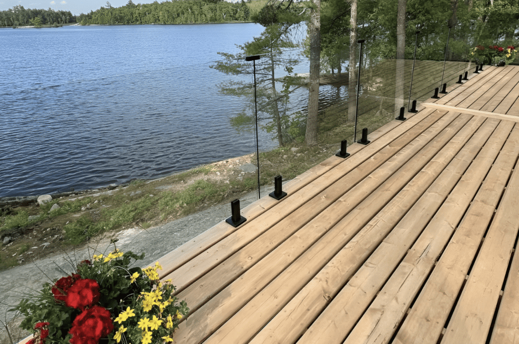Frameless glass deck railing with black spigots on wood lakefront deck with open lake view showing glass railing deck design