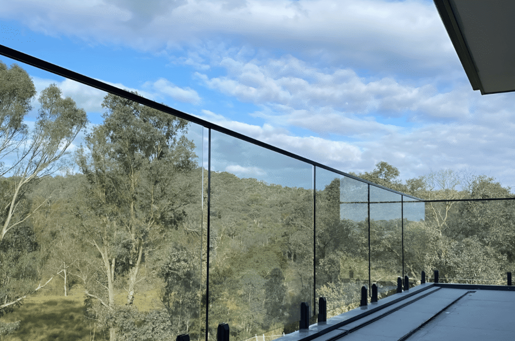 Panoramic forest view through frameless glass balcony railing with black top rail showing modern outdoor glass railing design