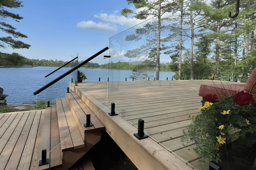Outdoor glass railing with black spigots and handrail along a lakefront wood deck and steps near a Seattle home