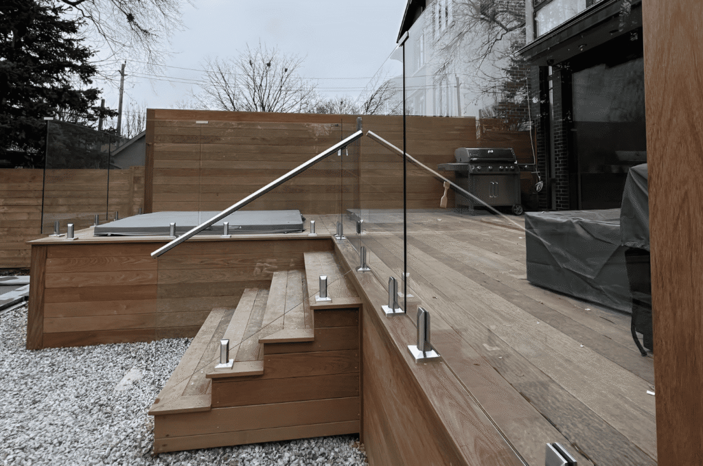 Tempered glass railing panels held by stainless steel spigots on a wood deck with steps, built for wet Seattle weather